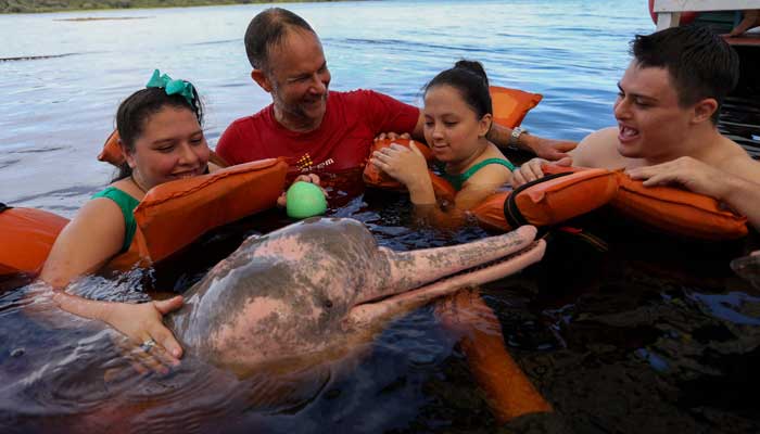 The physiotherapist Igor Simoes Andrade and young people with disabilities swim with pink dolphins (Inia Geoffrensis) in the Río Negro River in Iranduba, state of Amazonas, Brazil, on February 20, 2025. - AFP