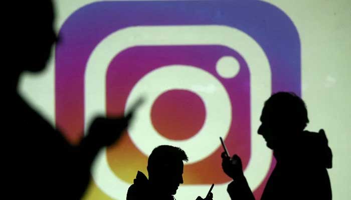 The silhouettes of mobile users are seen next to a screen projection of the Instagram logo in this image illustration taken on March 28, 2018. —Reuters