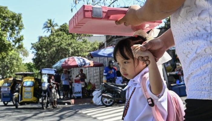 A man uses a school bag to protect a child from the sun when they leave school in Manila. - AFP/file