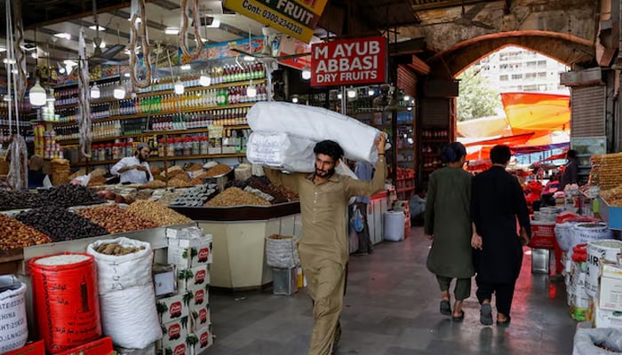 A man walks with bags on the shoulder to deliver to a nearby store in a market in Karachi, on June 11, 2024. - Reuters