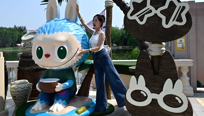 A woman poses for an image next to the Labubu character while visiting the Pop Mart Land theme park in Beijing, China, on June 18, 2025. - AFP