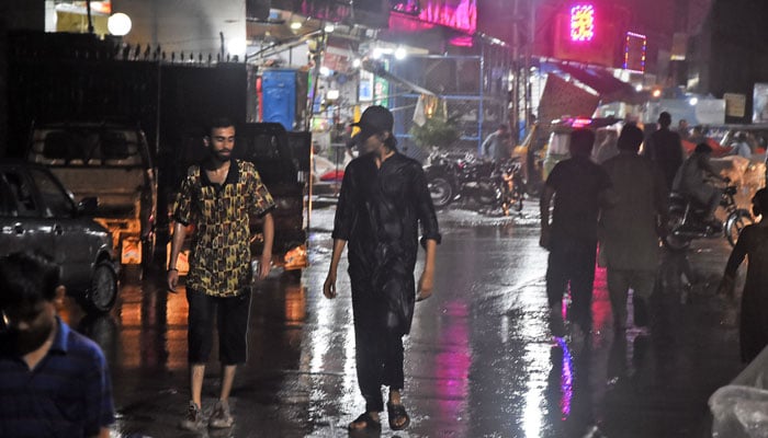 People make their way along a road while the heavy tabs of rawalpindi rain on June 22, 2025. - Online