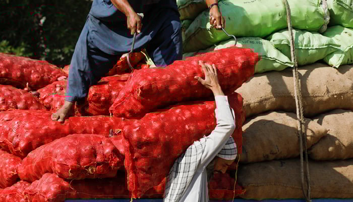 Workers download onion bags from a truck to supply in a market in Karachi, on February 1, 2023. - Reuters