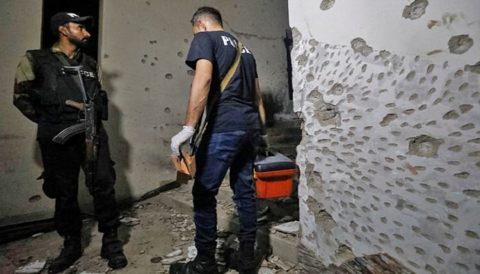 A member of the Forensic team passes by a police officer amid the damage after an attack on a police station in Karachi on February 17, 2023. - Reuters