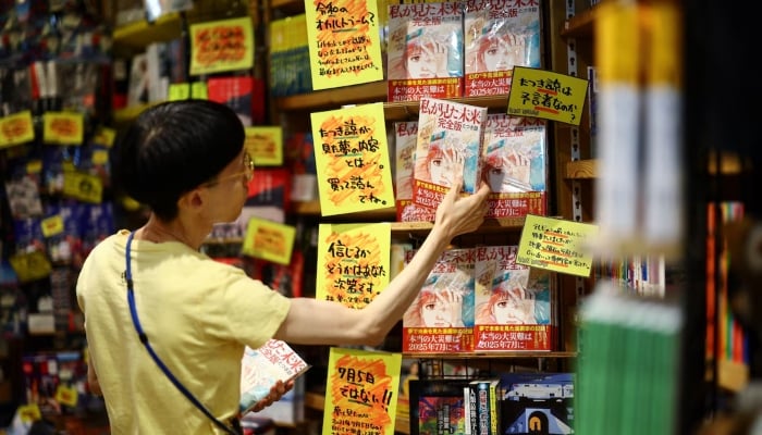 A staff member places the comic entitled The Future that I saw, written by manga artist Ryo Tatsuki, on the shelf in Village Vanguard Book Store in Tokyo, Japan, on June 30, 2025. - Reuters