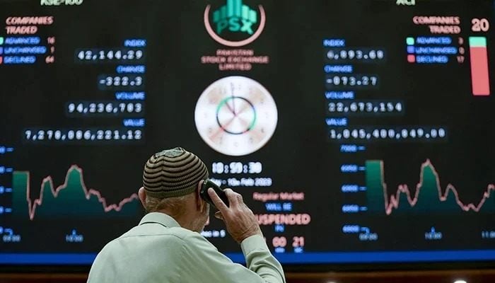 A corridor speaks on the phone while looking at an index plaque that shows the last prices of shares in the PSX in Karachi on February 10, 2023. - AFP