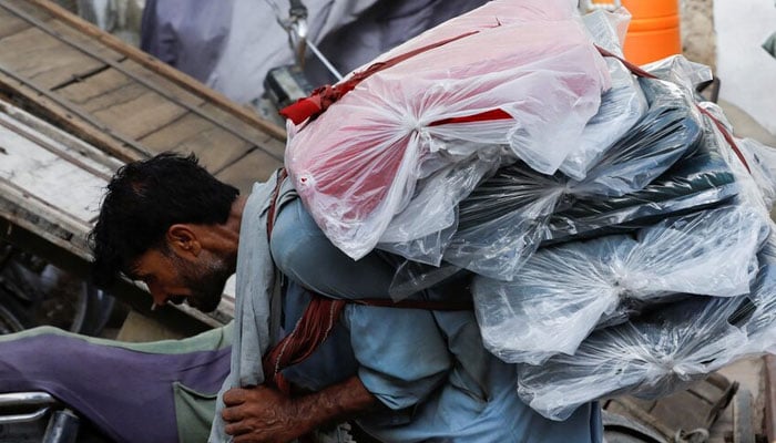 A worker leans while wearing textile fabric packages to deliver to a nearby store in a market in Karachi. - Reuters/file