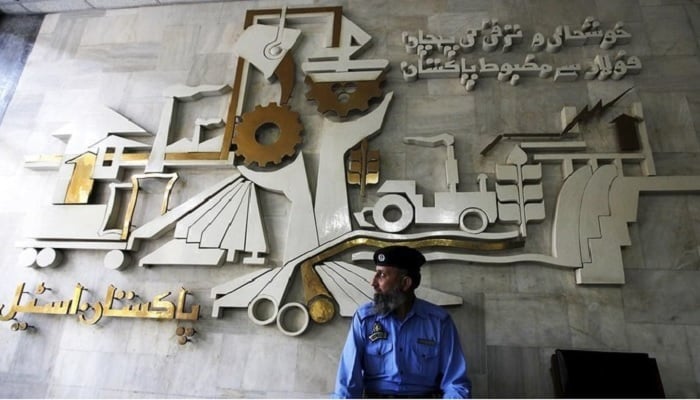 A security guard is in front of a wall with signs and slogans in the Building operation in Pakistan steel factories on the outskirts of Karachi.