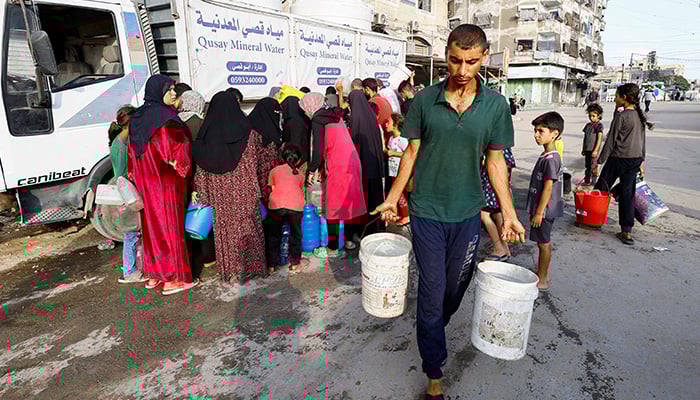 A man carries cubes of water while the Palestinians wait to collect water in the midst of shortage, in the city of Gaza, on August 6, 2025. - Reuters