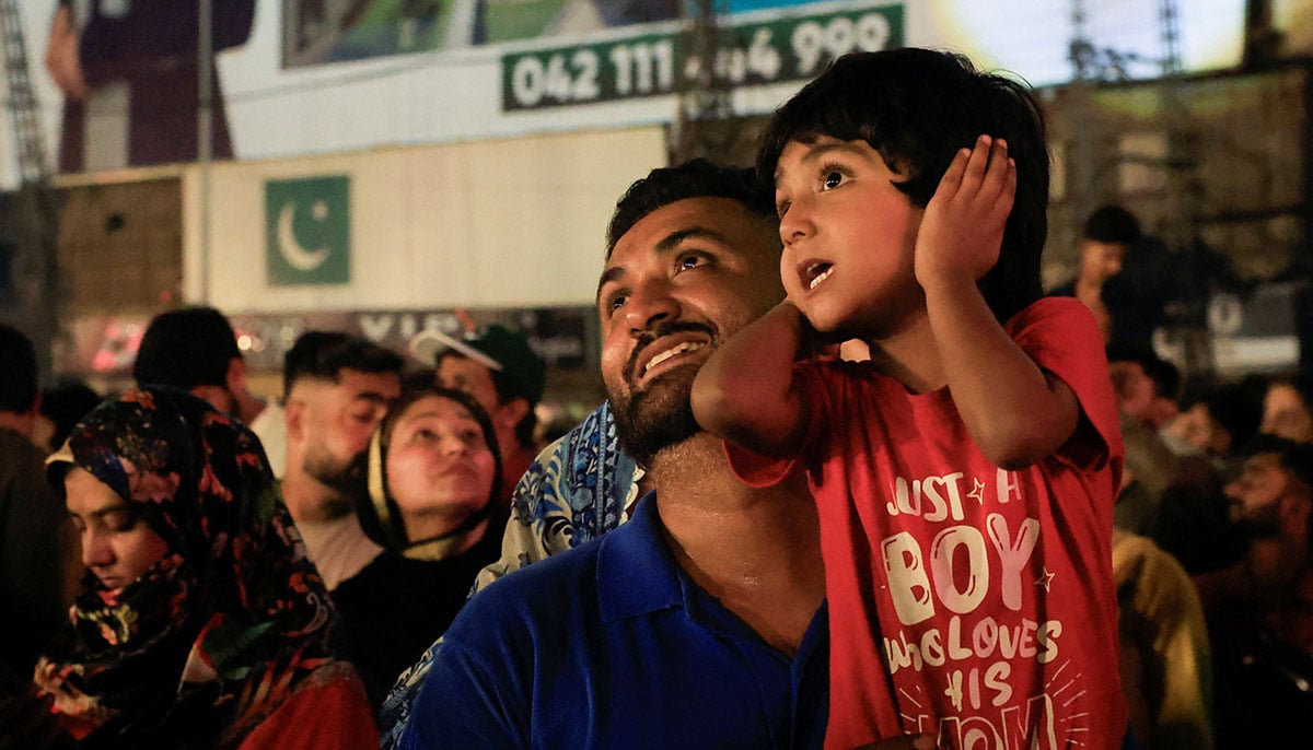 A child covers his ears while watching fireworks with his father during the celebration of Independence Day in Lahore on August 14, 2025. - Reuters