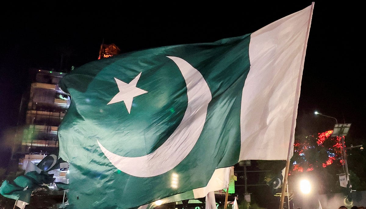 People greet national flags while they meet on the eve of Independence Day in Lahore on August 13, 2025. - Reuters
