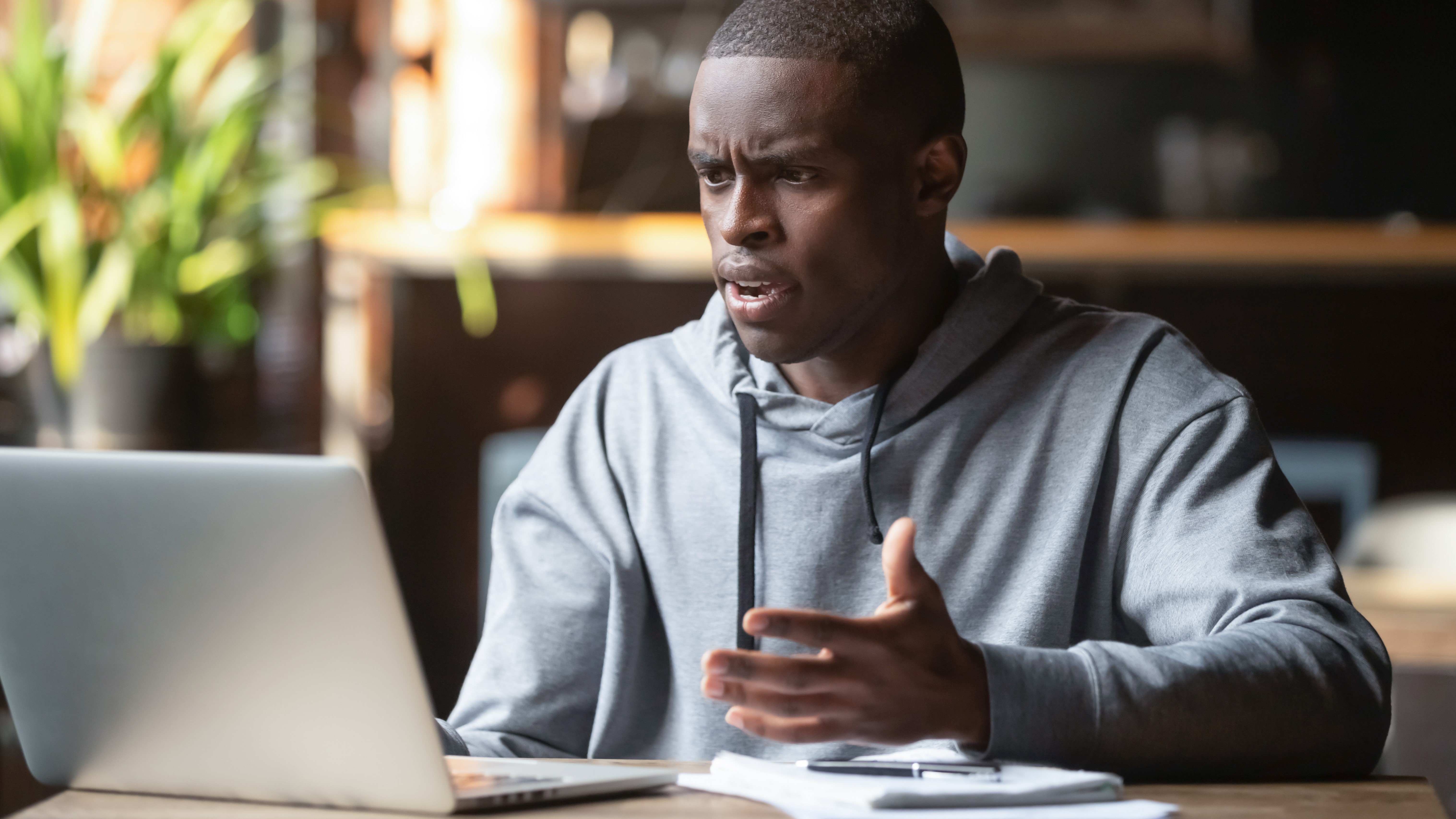 A man on a desk using a laptop and holding his hands up, while he had a confused look on his face