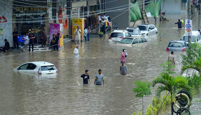 People walk on a road flooded with partially submerged vehicles after the rain of the monzón, in Karachi, Pakistan, August 19, 2025. - Reuters