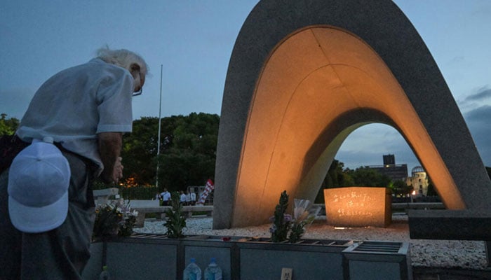 Visitors pray for the victims of the atomic bomb against the memorial cenotafio in Hiroshima. - AFP