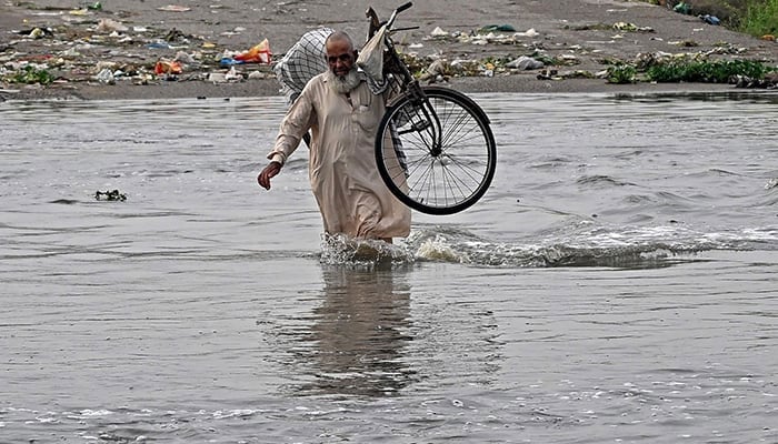 A man carries his bicycle while won by a road flooded after heavy monsoon rains in Karachi on August 20, 2025. - AFP
