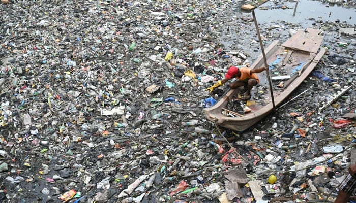 A municipal worker clears the plastic and garbage waste drowning the water flow of the Buckingham channel in Chennai in November 2023. - AFP