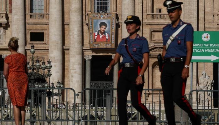 Carabinieri walks next to a tapestry that hangs from the facade of the Basilica of St. Peters in the Vatican that represents an image of Carlo Acutis, an Italian child born in British that will become the first millennium that becomes a Catholic saint in a ceremony directed by Pope Leo, as seen from Rome, Italy, September 4, 2025.