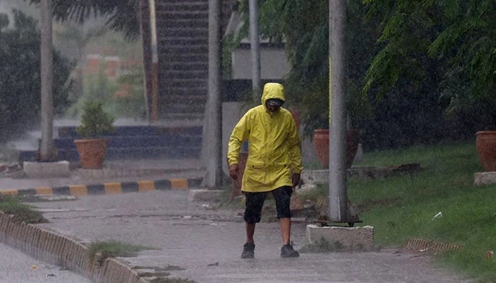 A man wears a rain jacket while walking on a sidewalk during a rain in Karachi, Pakistan, August 2, 2024. - Reuters