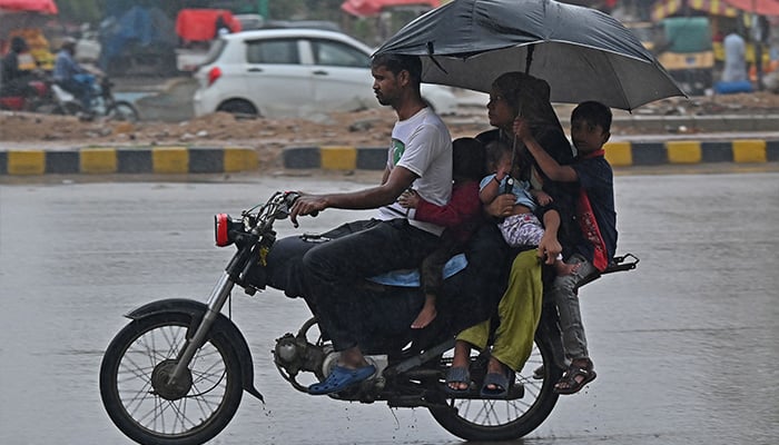 A family riding a motorcycle along a street during the rain in Karachi on September 9, 2025. - AFP