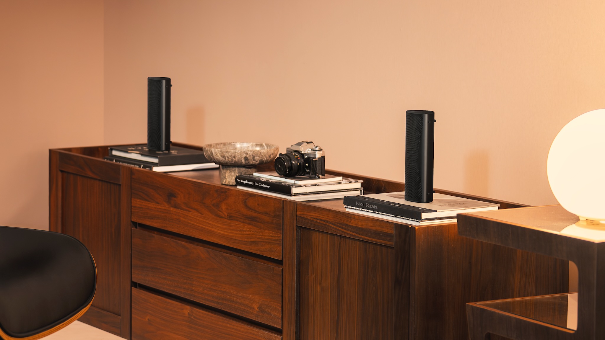 Image of two muo speakers on a wooden desk with a camera between them and books under them