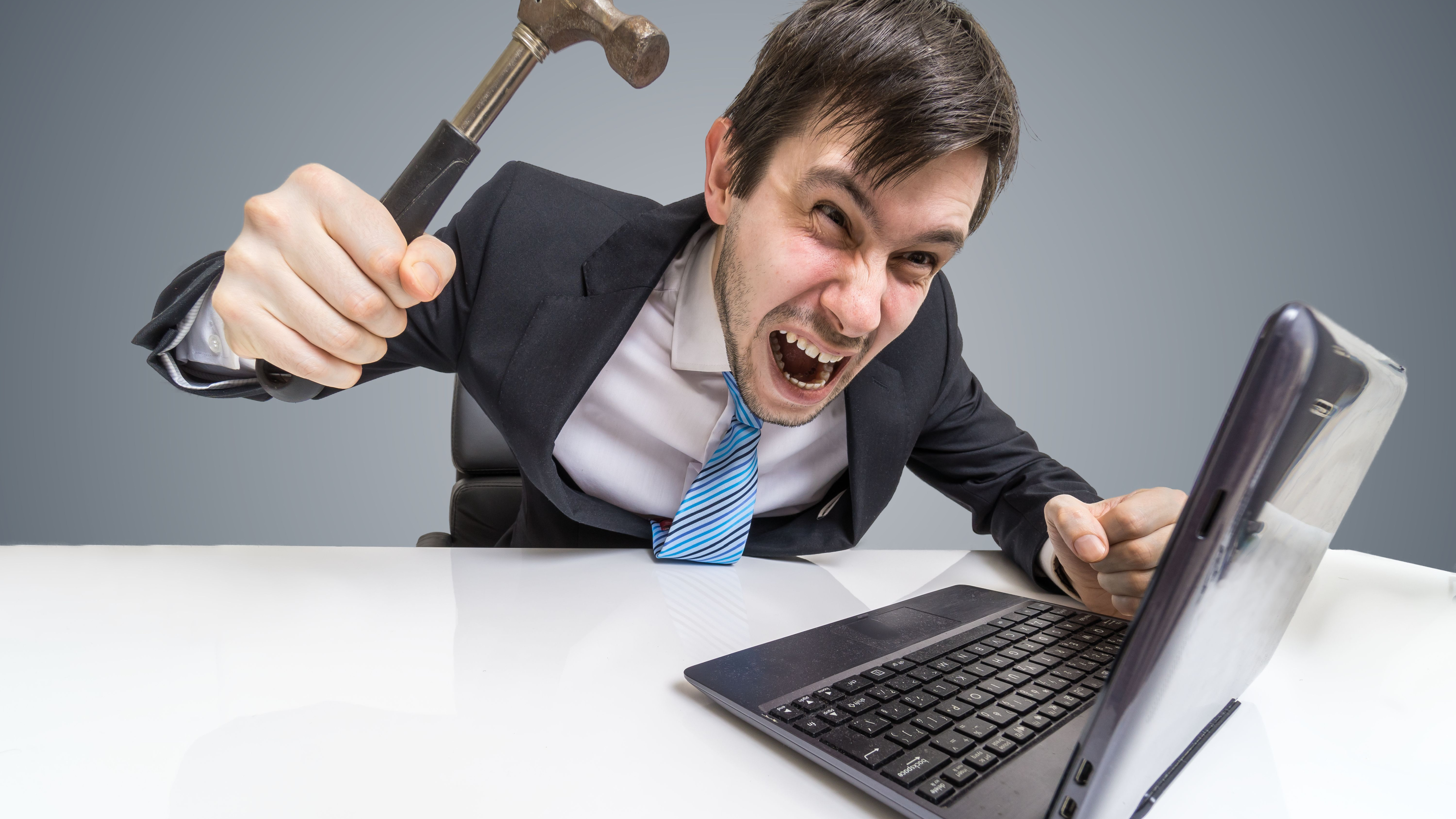 The angry and crazy man is working with the laptop. You will damage the notebook with Hammer.