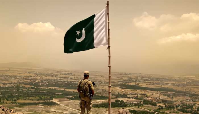 A soldier looks towards a vast land area with the Pakistani flag that flutter over his head in this still taken from a video. - YouTube@ispr of the official