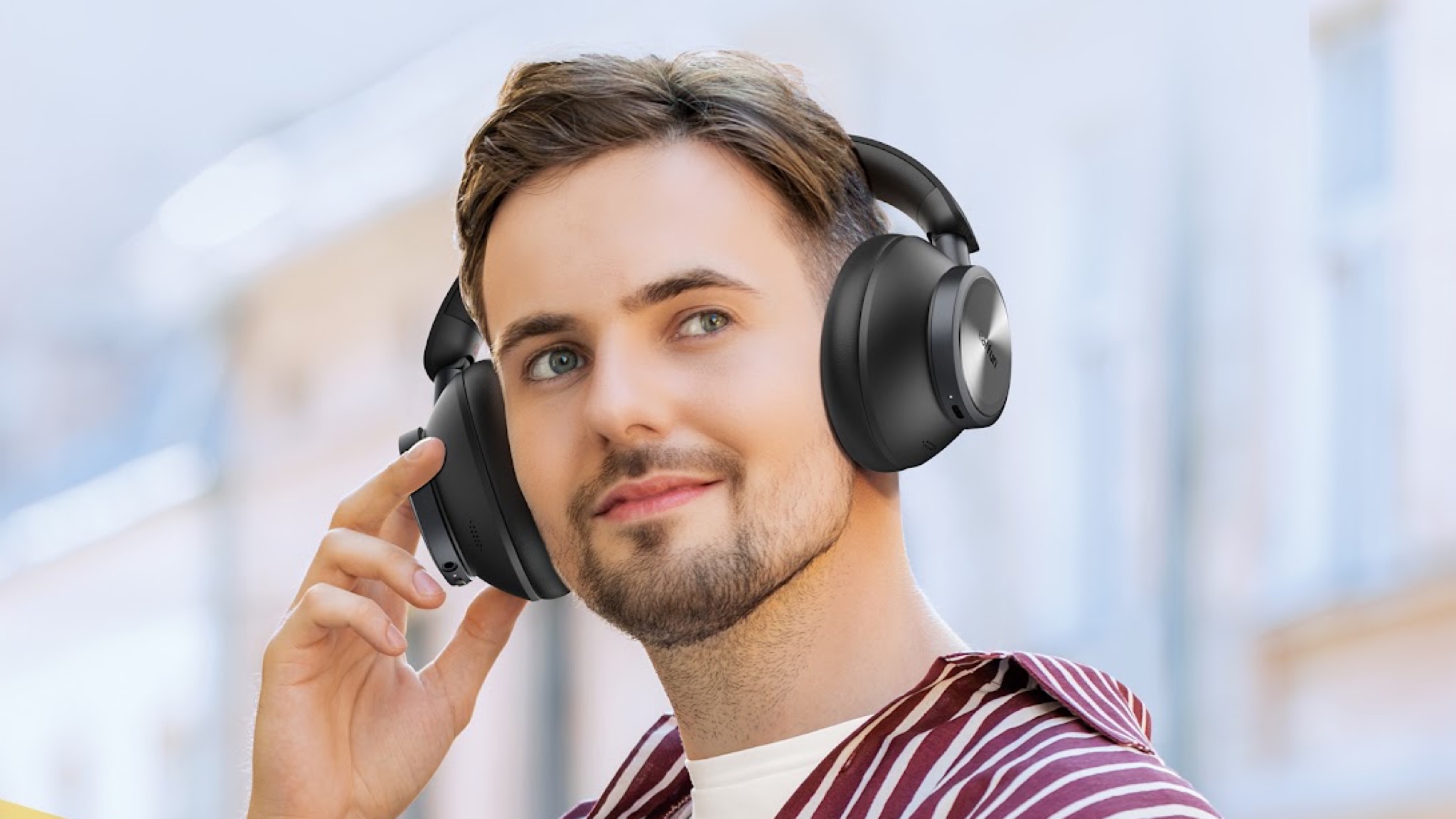 A man with dark hair and knob beard is listening to a couple of Earfun Wave Pro X headphones