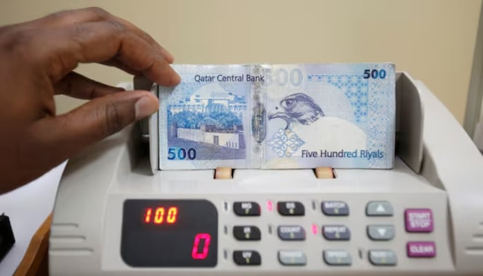A cashier has notes of Qatari Riyal in a money changer on Doha May 28, 2013. - Reuters