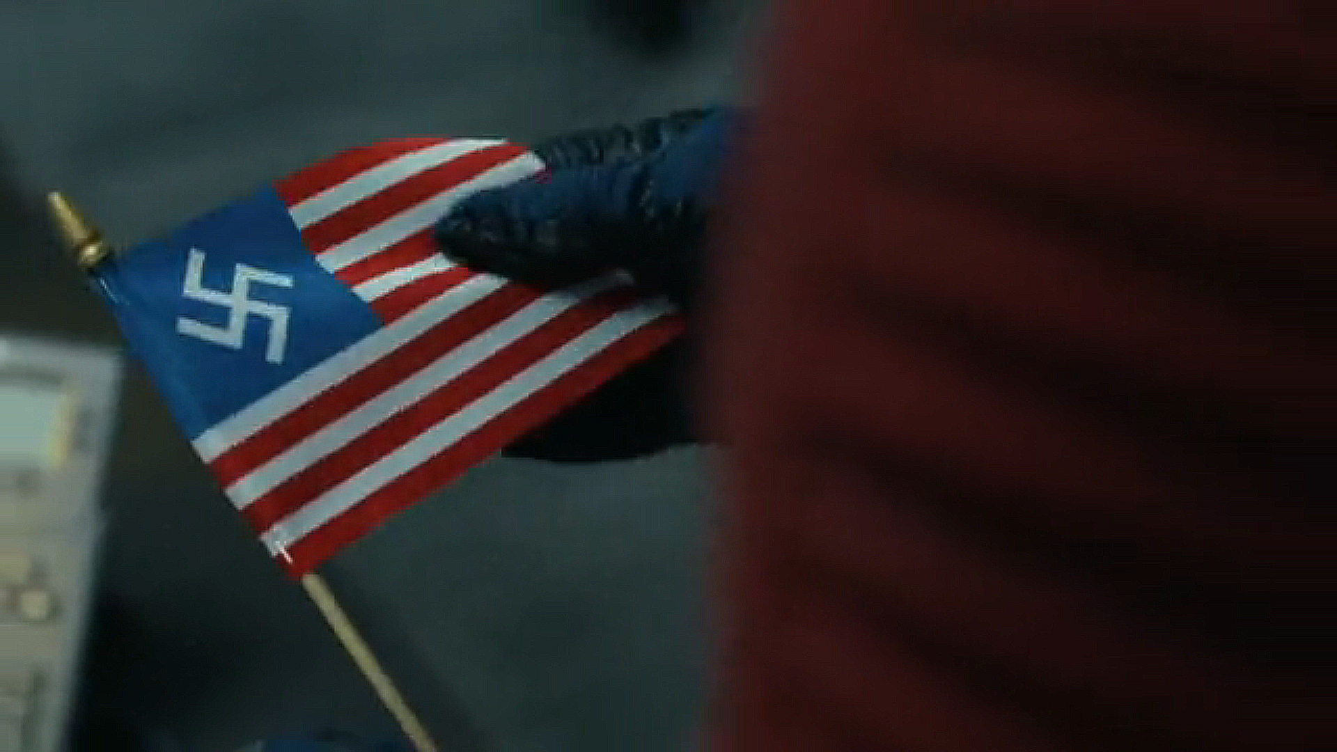 A close -up of Chris Smith holding a US Nazi flag. Uu. In Peacemaker season 2 episode 6