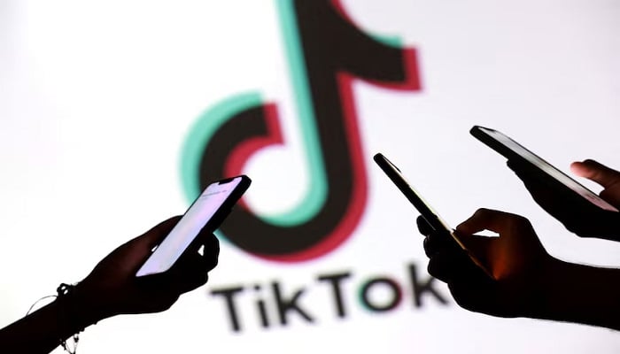Teenagers pose for a photo while sustaining smartphones in front of a Tiktok logo in this illustration taken on September 11, 2025.