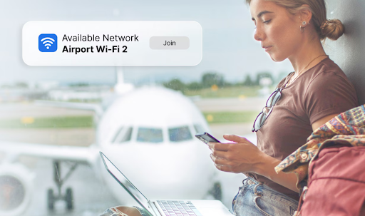 A woman sits at the airport, using a laptop and a phone connected to Wi-Fi