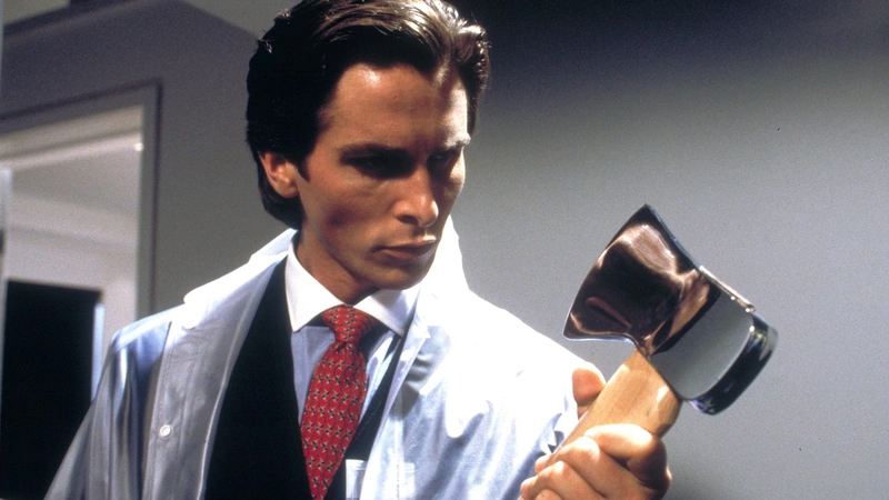 A still from the movie American Psycho in which Patrick Bateman (Christian Bale) carries a suit and looks at an ax.