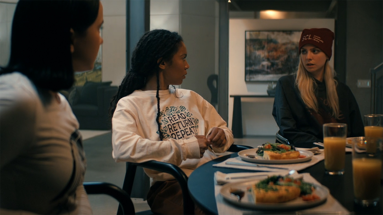 Jordan and Marie look at Cate as they sit at a table full of food on Gen V season 2, episode 6.