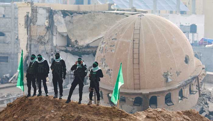Hamas fighters stand guard during the handover of deceased hostages in the southern Gaza Strip, February 2025. – Reuters