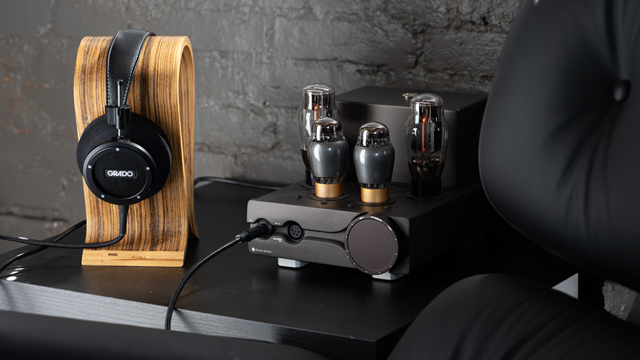 Grado Signature S750 headphones on a wooden stand next to a dark headphone amplifier with large tubes protruding from the top