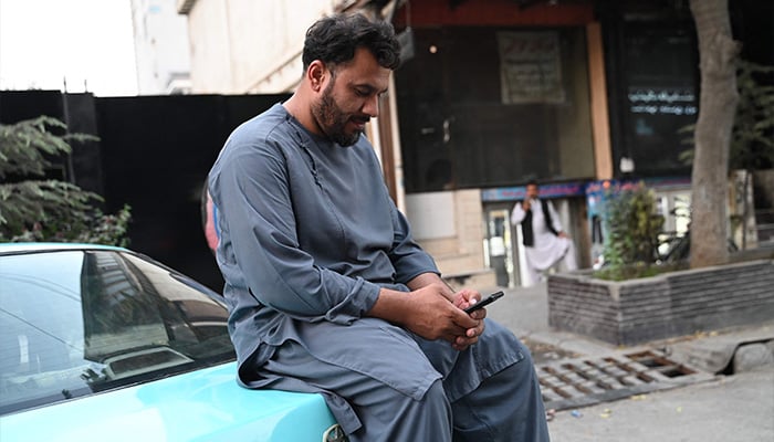 An Afghan taxi driver uses his mobile phone while he sits in his vehicle along a street in Kabul on October 1, 2025. - AFP