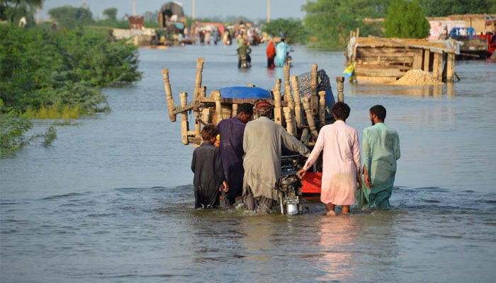 Men walk along a path flooded with their belongings, after rains and floods during the monzón season in Sohbatpur, Pakistan, on August 28, 2022. - Reuters