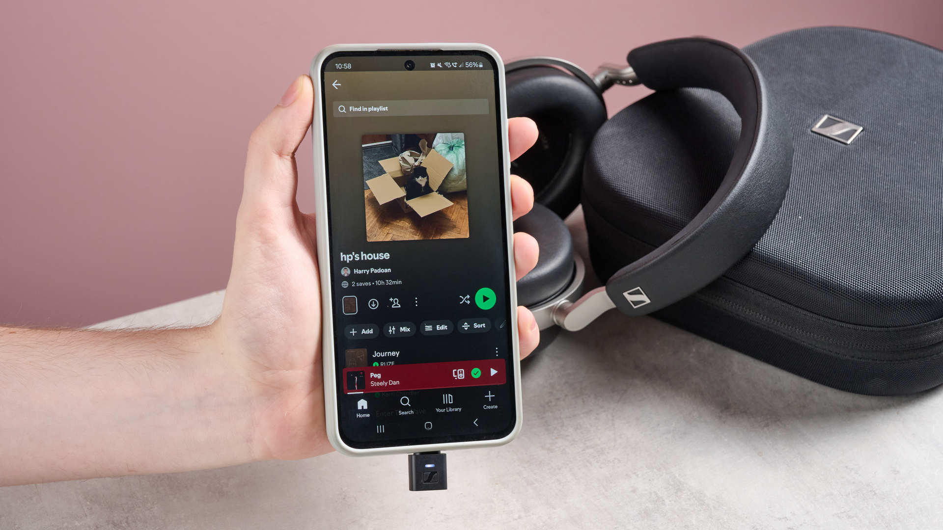 Person holding a phone with Spotify on in front of Sennheiser HDB 630 and a carrying case