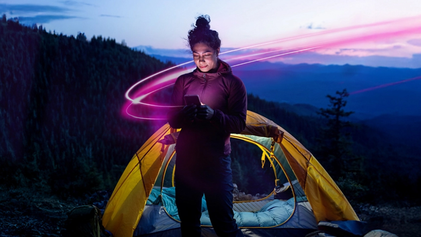 A woman stands in front of a tent using the T-Mobile satellite Internet service