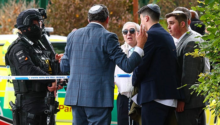 Armed Police officers talk to community members near the Heaton Park Congregation Synagogue in Crumpall, North Manchester, on October 2, 2025, after an incident in the synagogue. - AFP