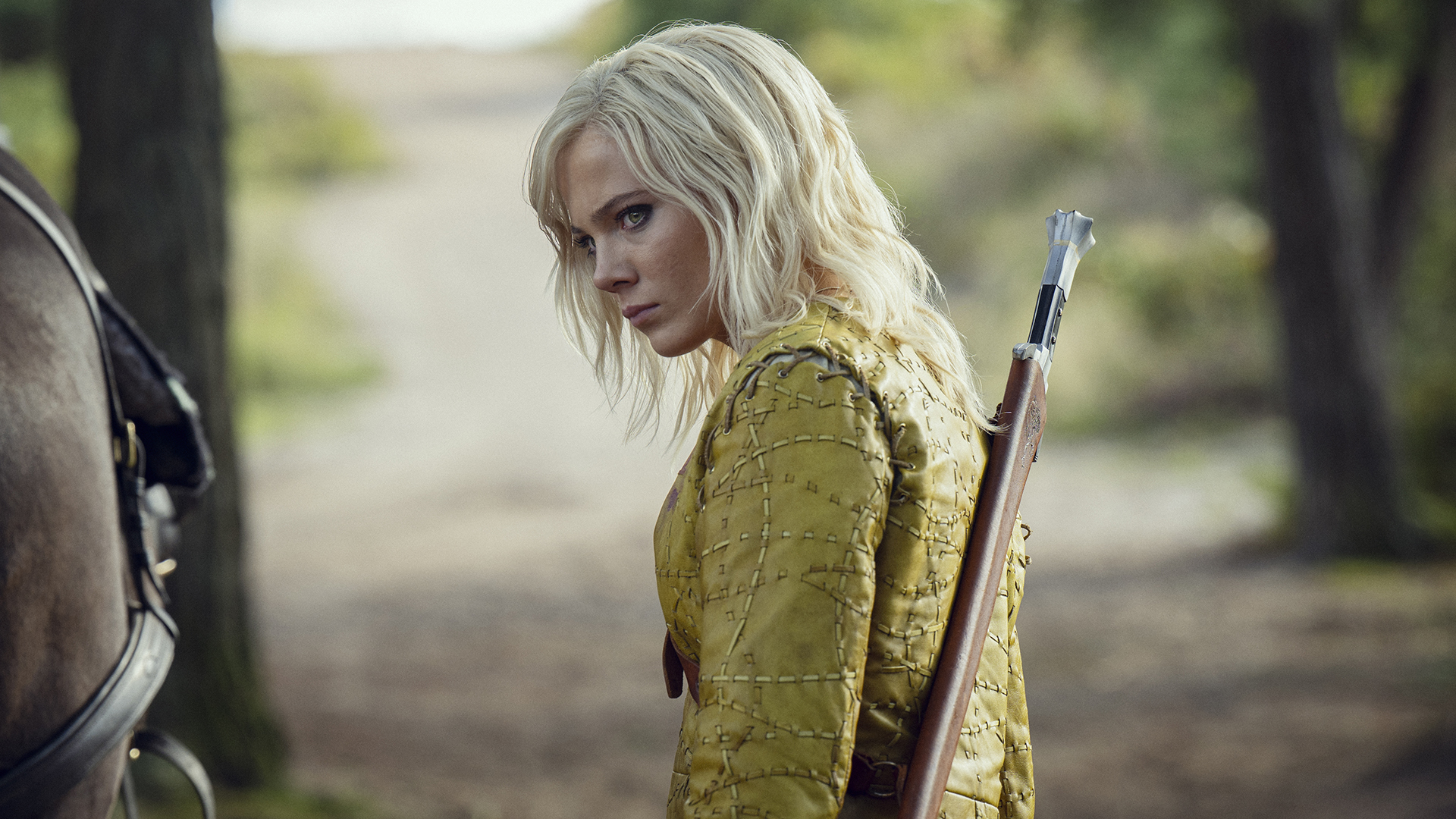 Ciri wearing a mustard yellow top and a sword hanging from her back in season 4 of The Witcher.