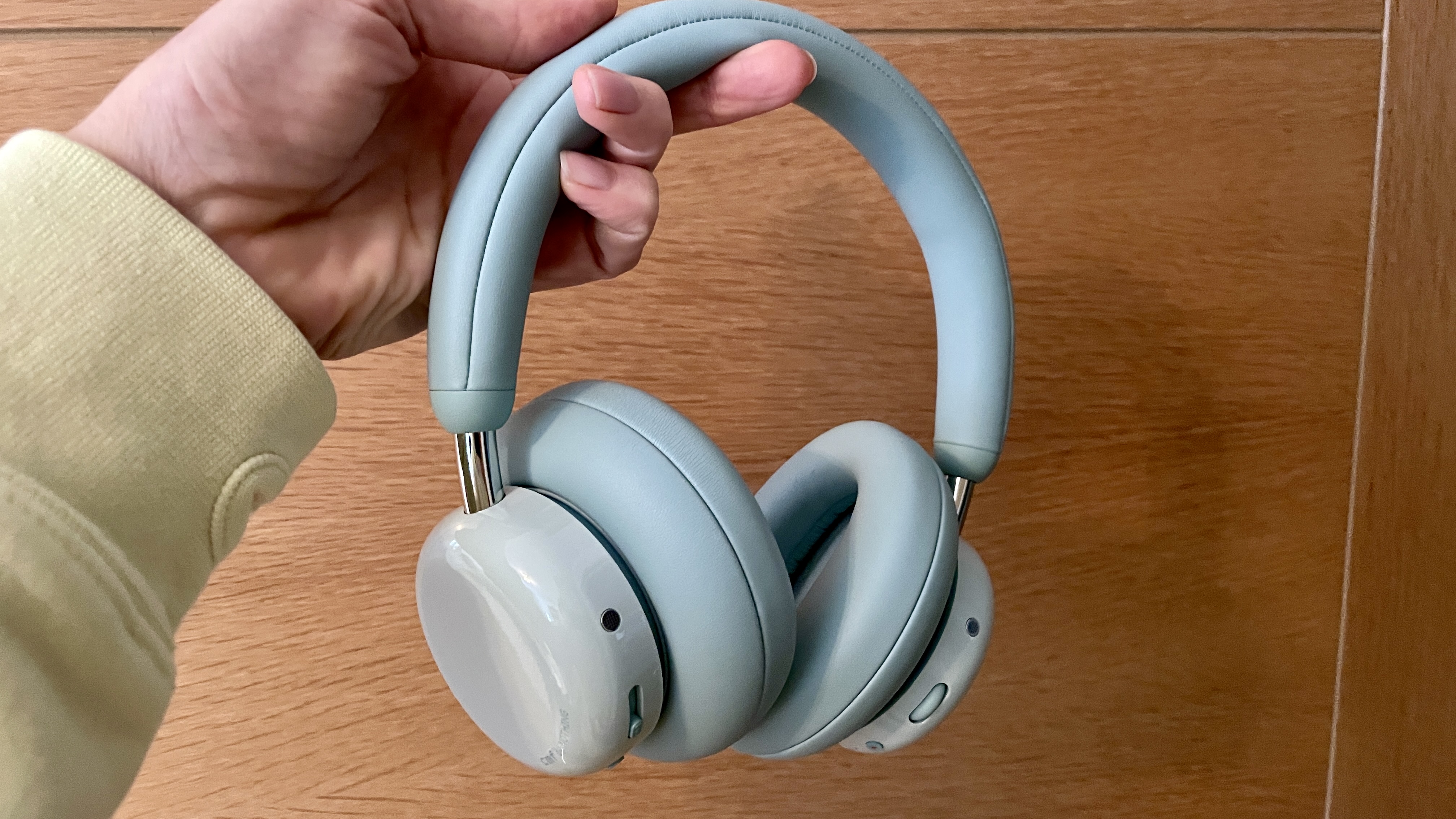 CMF Headphone Pro in pistachio green held in one hand or hanging from a bar, pushed up by a carved frog