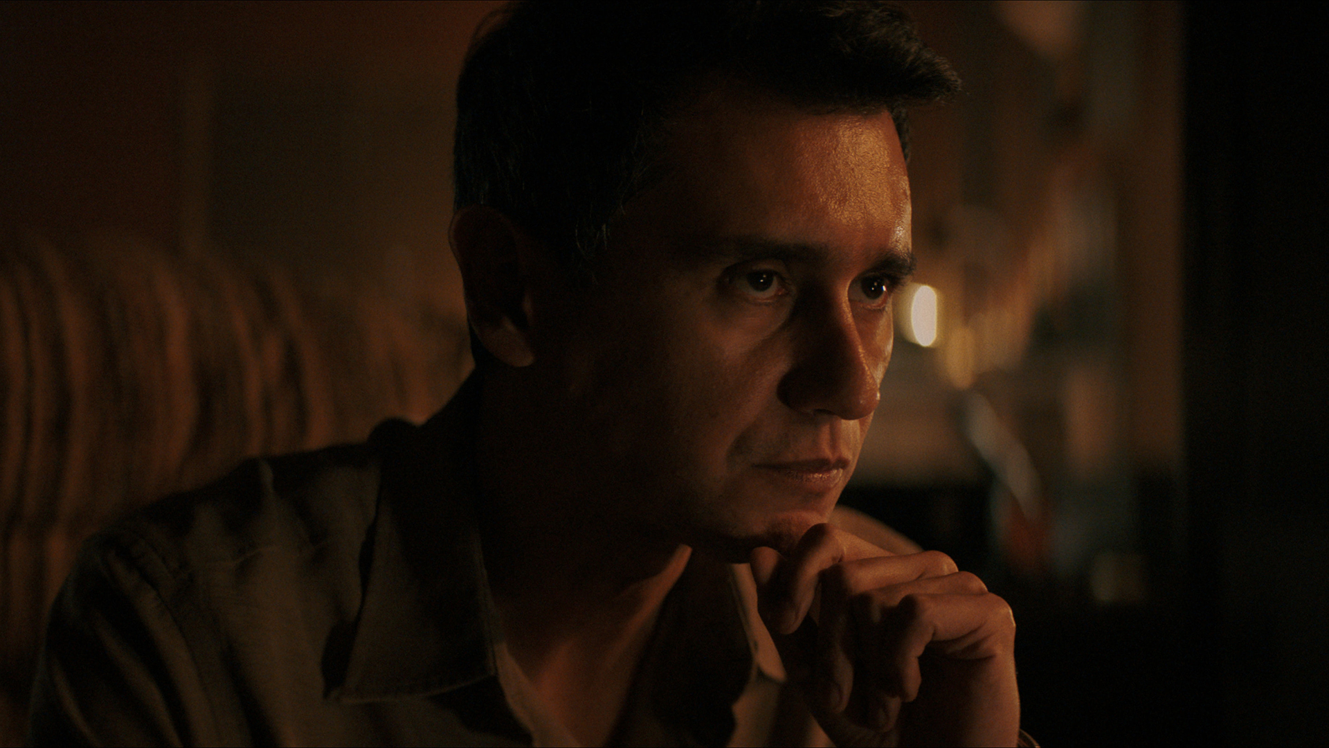 Manusos resting his chin on his left hand in episode 4 of Pluribus