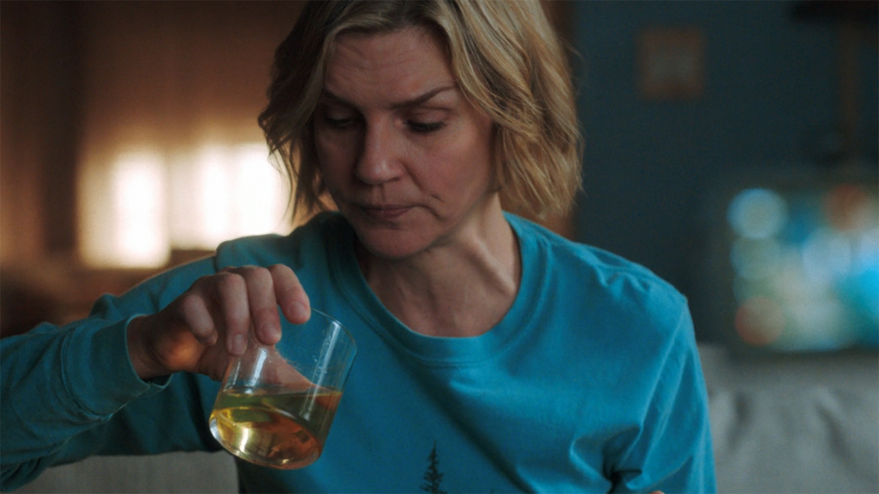 Carol sitting and looking at an orange liquid in a glass in episode 5 of Pluribus