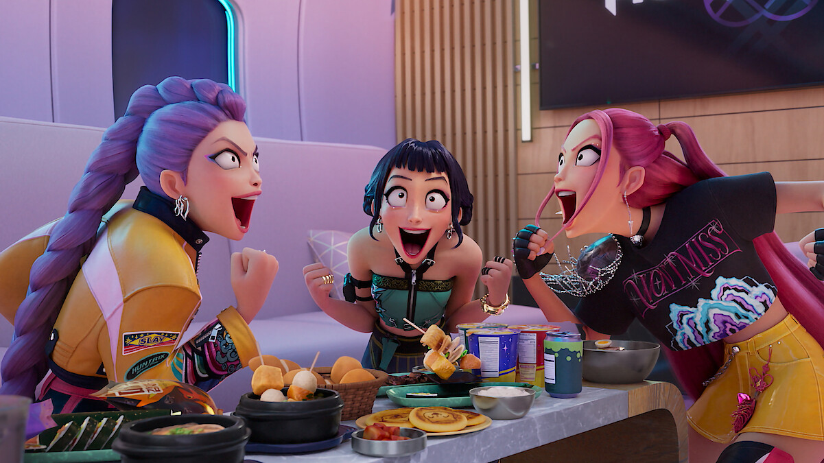 Rumi, Zoey and Mira cheer while sitting at a table full of food in Kpop Demon Hunters.