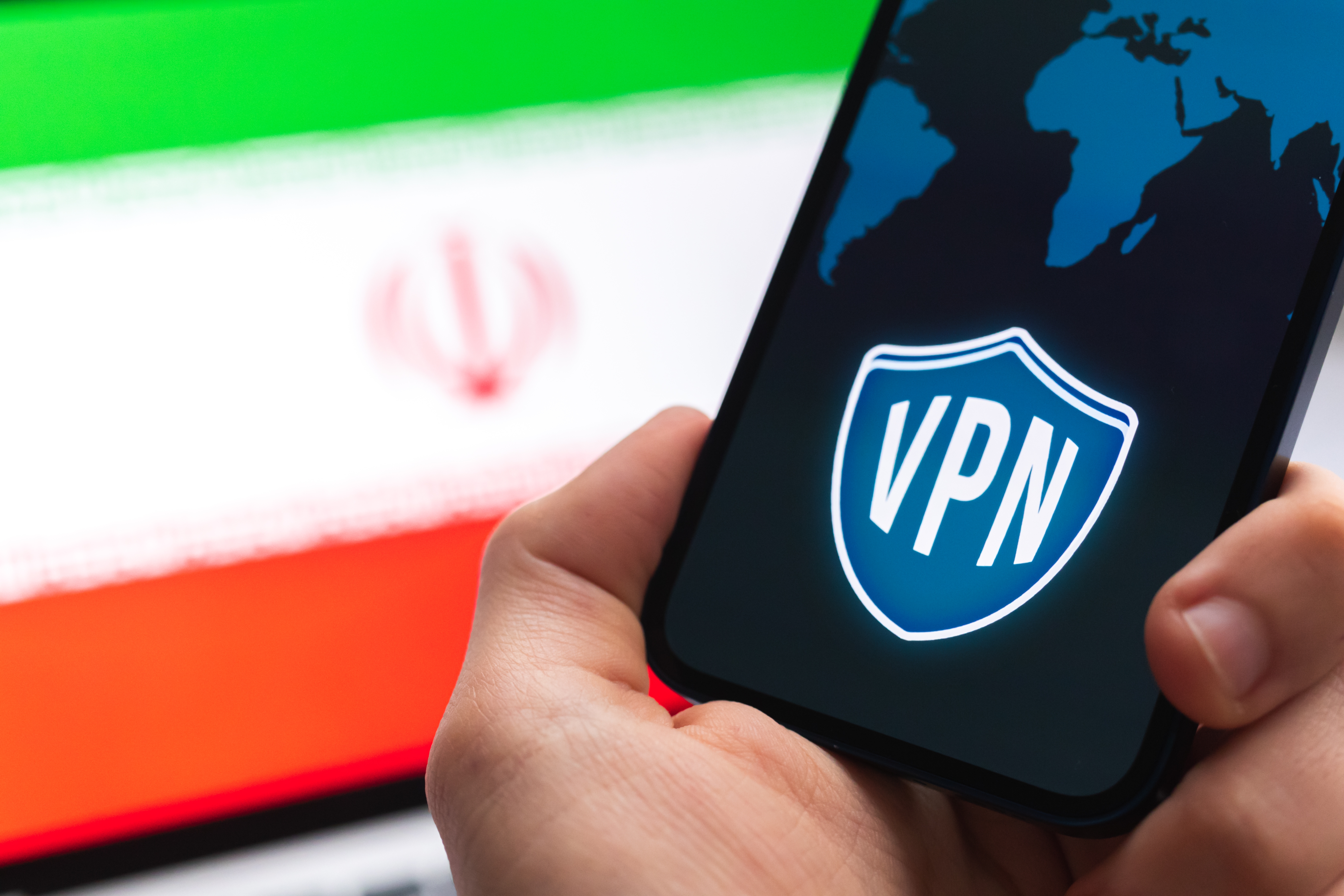A hand with a mobile phone and a VPN application in front of the flag of Iran