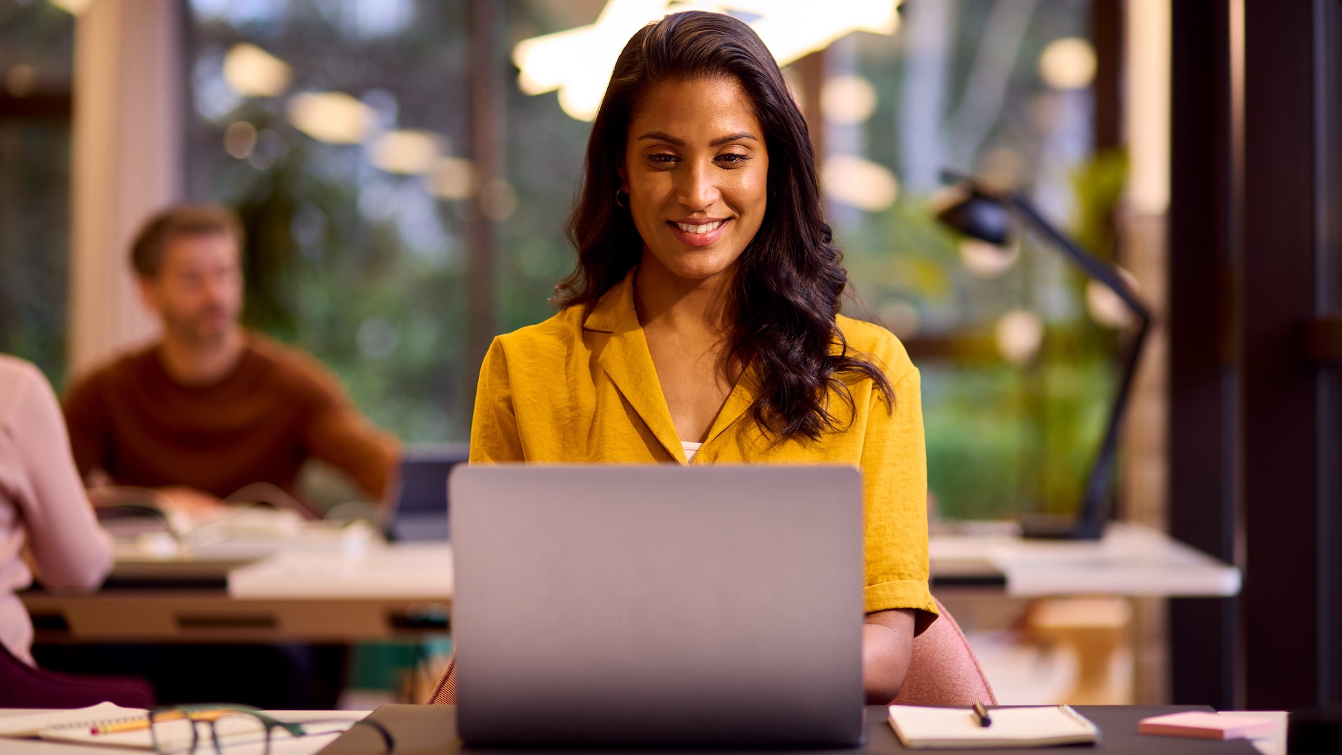 A young woman is working on a Windows 11 laptop in a relaxed office space and looks happy