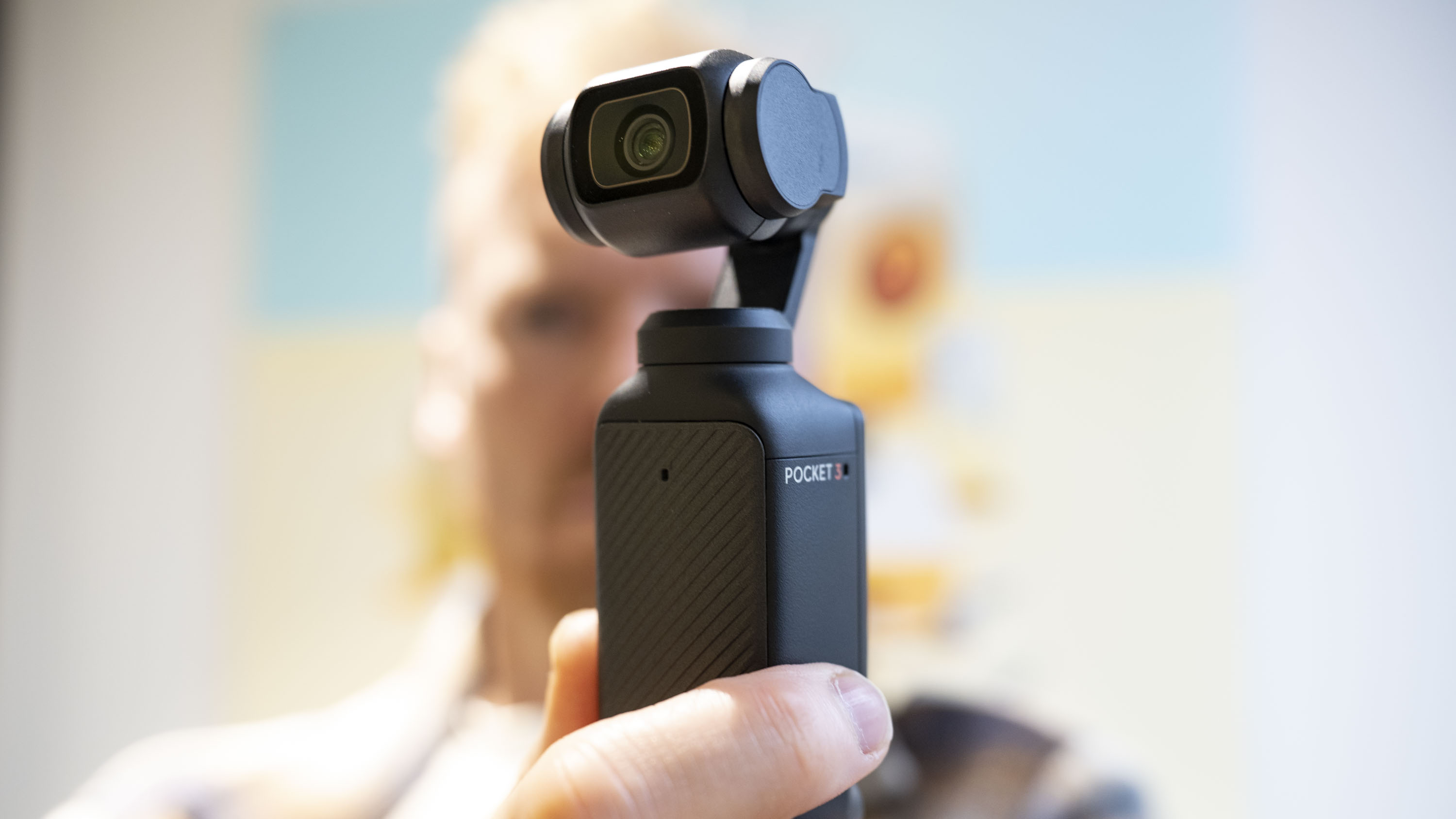 DJI Osmo Pocket 3 vlogging camera in the user's hand, with them blurred in the background