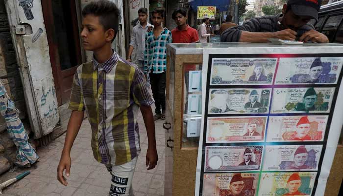 A boy walks past a sidewalk currency exchange stall decorated with photographs of banknotes in Karachi. — Reuters/Archive