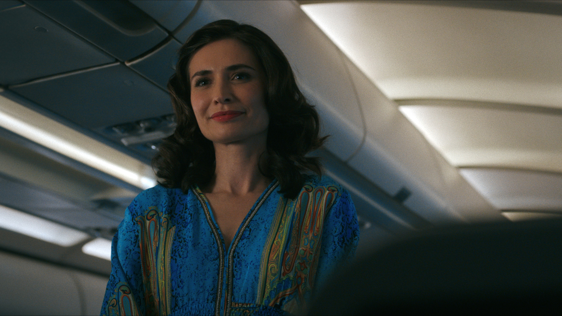 Zosia standing and smiling on a plane in episode 3 of Pluribus